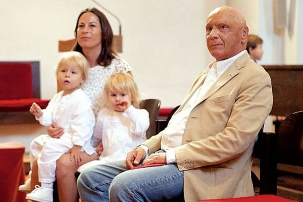 Birgit is wearing white dress as her twins children are wearing same and her husband is wearing cream coat with blue jeans and white shirt.